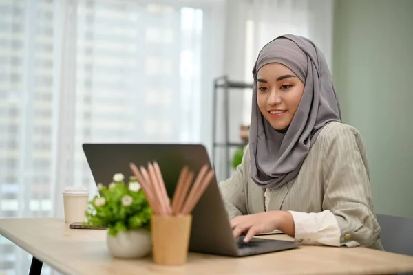 stock image Attractive and professional millennial Asian Muslim businesswoman wearing hijab working in the office, using notebook laptop computer.