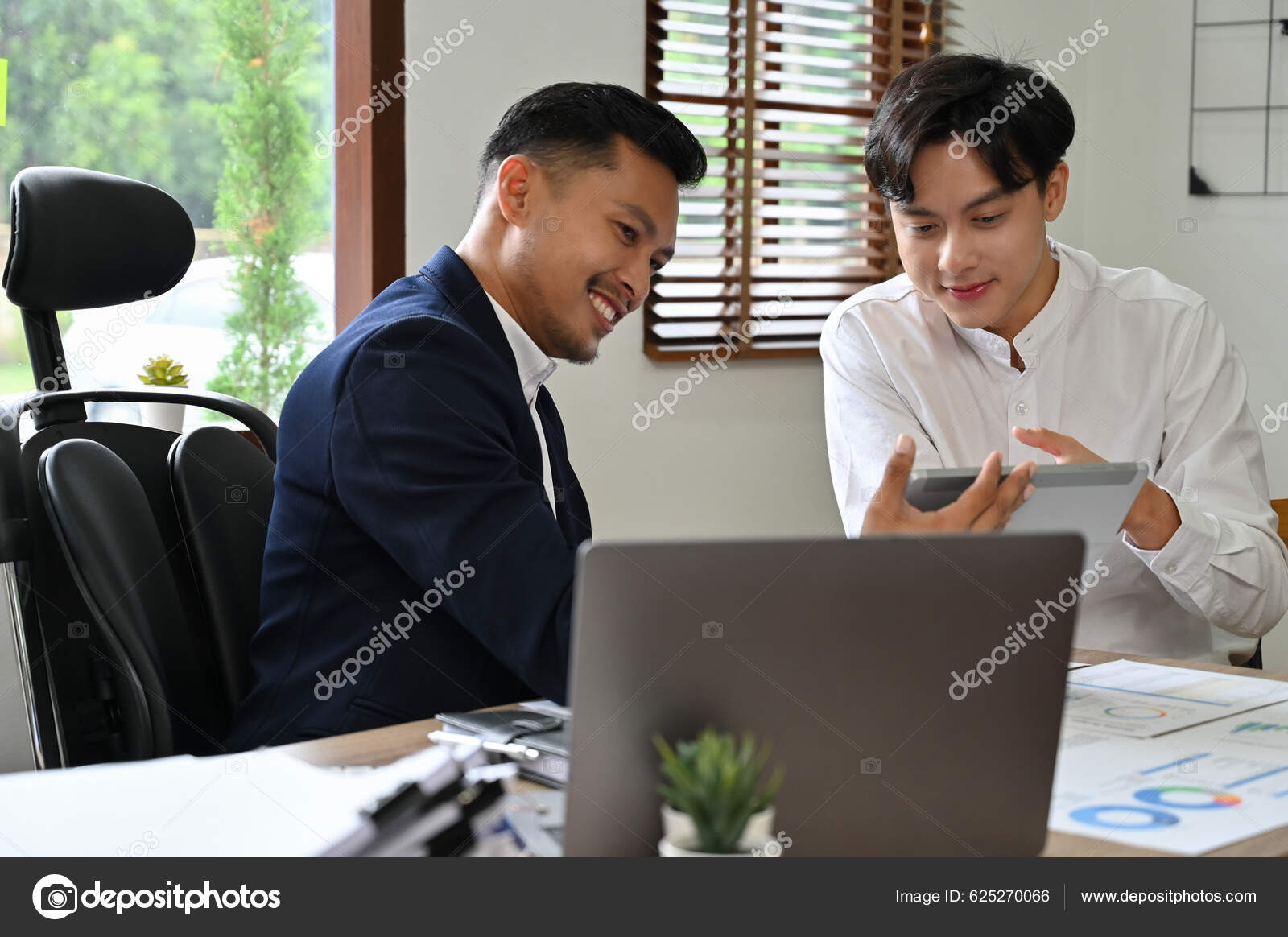 聪明的年轻亚洲男性金融分析师或金融工作者向办公室的男性老板展示并解释他的金融分析数据——图库图片© BongkarnGraphic #625270066