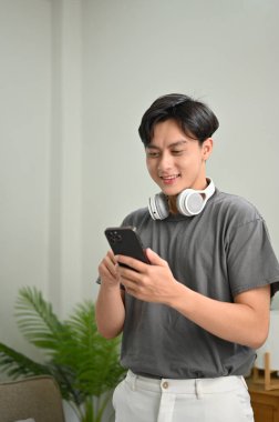 Portre, kablosuz kulaklıklı yakışıklı Asyalı genç, akıllı telefonunu arkadaşlarıyla sohbet etmek için kullanıyor..