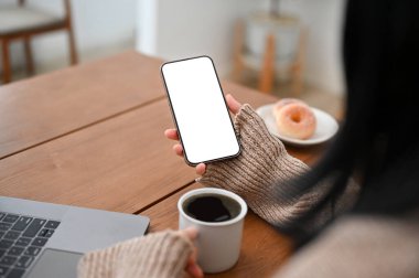 Akıllı telefonunu internet haberleri ya da içerikleri okumak için kullanan Asyalı bir kadın. Kahvesini yudumluyor, kafede uzaktan çalışıyor. Kesilmiş görüntü.