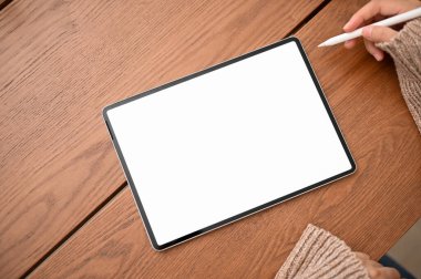 Üst manzara, dijital tablet dokunmatik kâğıdına stilus kalem çizen bir kadın. Tablet beyaz ekran modeli ahşap masanın üstünde.