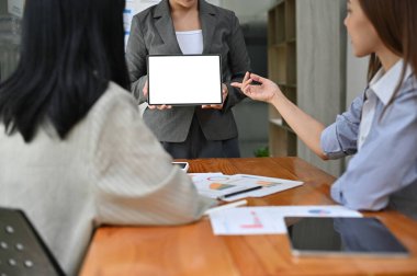 Asyalı bir kadın pazarlama çalışanı, pazarlama projesi kampanyasını toplantıda ekibine sunmak için bir tablet kullanıyor. Tablet beyaz ekran modeli. kırpılmış atış