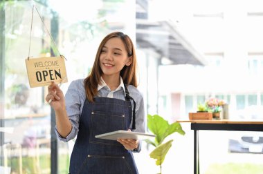 Milenyum Asyalı güzel bayan garson ya da önlüklü garson restoran girişinin önünde tabletiyle duruyor. Küçük işletme sahibi kavramı