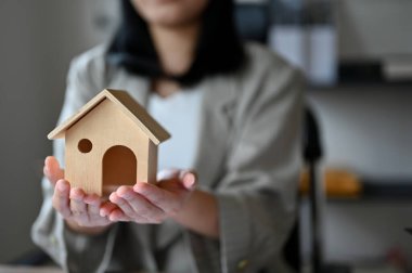Profesyonel Asyalı kadın emlakçı ya da emlakçı elinde bir ev modeli gösteriyor. Kiralık ev, emlak yatırımı. kırpılmış ve yakın plan resim