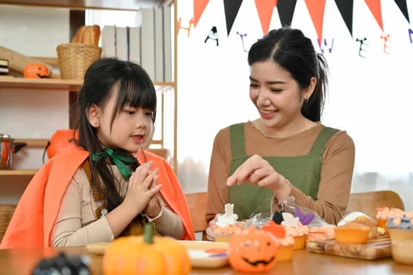 身穿万圣节服装的快乐可爱的年轻亚洲女孩喜欢在家里和妈妈一起装饰杯子蛋糕 万圣节快乐假期的概念 — 图库照片