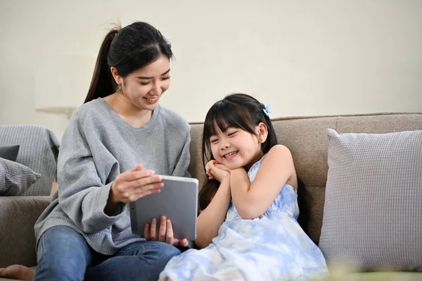 아름답고 아시아인 엄마가 딸에게 태블릿으로 뭔가를보여 주면서 아이들의 만화를 보면서 — 스톡 사진