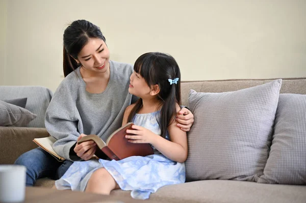 아름답고 스러운 아시아 엄마가 읽거나 귀여운 딸에게 거실에서 휴식을 취하는 — 스톡 사진