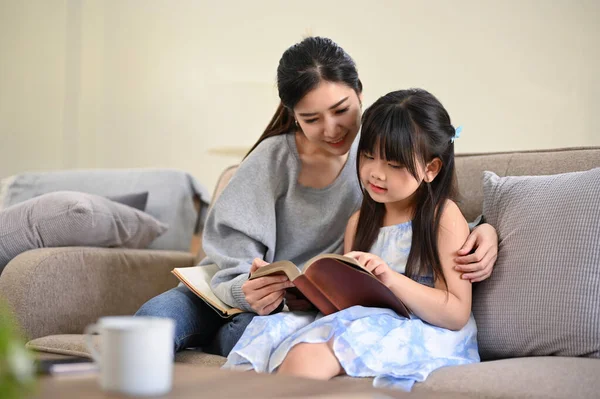 편안하고 스러운 아시아인 어머니 거실에서 편안하게 쉬면서 읽거나 귀여운 딸에게 — 스톡 사진