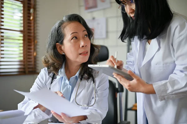 Professional senior Asian female doctor showing and explaining an advance medical information on the research to her assistant.