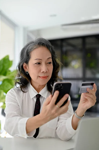 stock image Portrait, Happy Aged Asian businesswoman holding her smartphone and a credit card, using mobile banking application. cashless payment concept