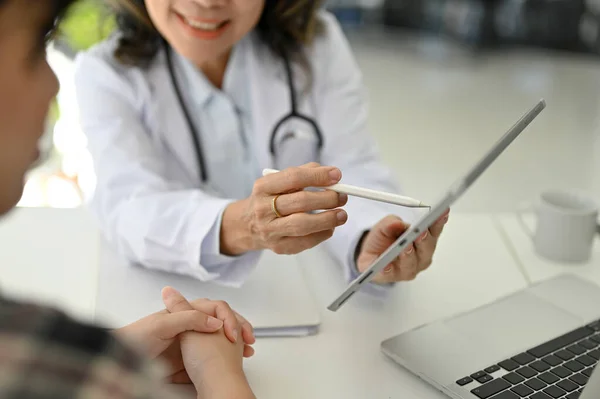 Professional and cheerful Asian aged female doctor explained the treatment plan and gave instructions for the patient's medicine prescription during the appointment. cropped image