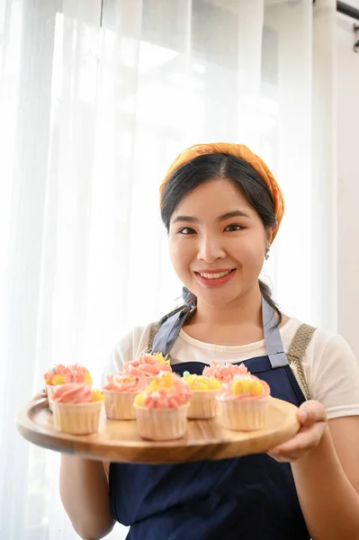 Mujer Joven Sosteniendo Cupcake Terminado Bandeja Madera Mano Sonriendo Cámara —  Fotos de Stock