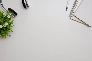 Üst görünüm, kulaklıklı beyaz çalışma alanı, not defteri, kalem, dekor bitkisi ve metin görüntüleme alanı