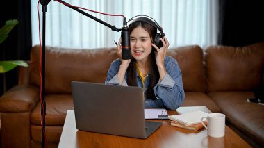 Güzel ve çekici genç Asyalı kadın serbest radyo yayını sunucusu oturma odasından kulaklıklar ve mikrofonla şovunu yönetiyor. Podcast konsepti