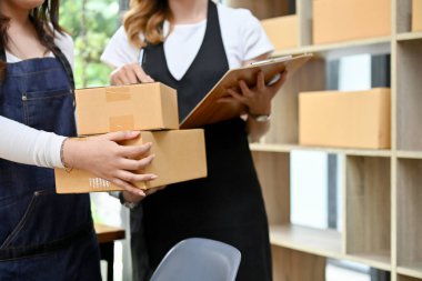 İki genç Asyalı bayan küçük işletme girişimcisi depodaki nakliye kutularını ve ürün stoklarını birlikte kontrol ediyorlar. kırpılmış resim