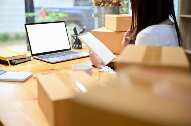 Meşgul ve başarılı Asyalı kadın e-ticaret şirketi. Ev ofisinde çalışıyor, nakliye paketlerini hazırlıyor ve online siparişleri kontrol ediyor..