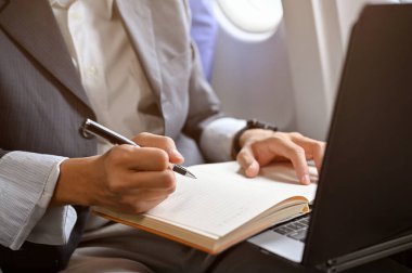 Bir iş adamı not defterine not alıyor, dizüstü bilgisayar kullanıyor, iş seyahatleri sırasında iş görevleri üzerinde çalışıyor. kırpılmış ve yakın plan el resmi