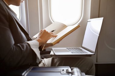 Profesyonel genç Asyalı işadamı uçakta, defterine bir şeyler okuyor, kontrol ediyor ya da yazıyor. kırpılmış ve yakın plan resim