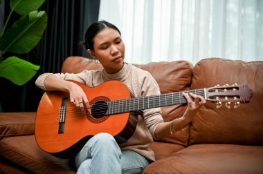 Modern klasik oturma odasında akustik gitarını çalarken binlerce yıllık Asyalı kadın şarkı söylüyor. Hobi ve eğlence konsepti