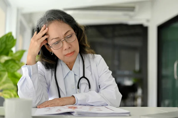 紧张的亚洲老年女医生在她的写字台工作时头痛或偏头痛 — 图库照片