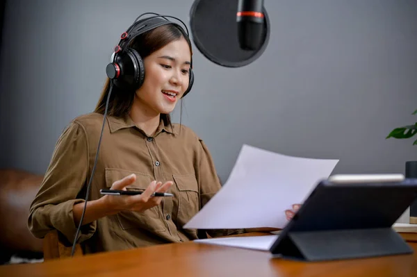 stock image Talented young Asian female freelance blogger or radio host reading her podcast script and running her online radio channel in her studio.