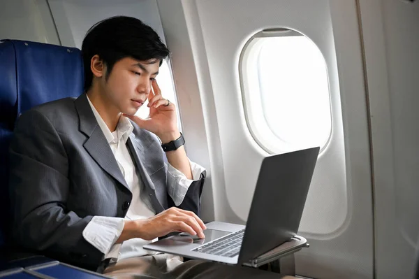 Professional and successful young Asian businessman or male executive manager in formal suit working on his project, using laptop computer during the flight to his business meeting.