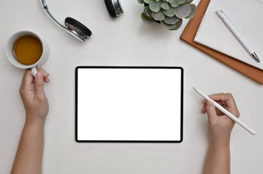 Üst görünüm, minimalist beyaz ofis masasında çalışan, dijital tablet kullanan ve kahvesini yudumlayan bir kadın grafik tasarımcısı. tablet beyaz ekran modeli
