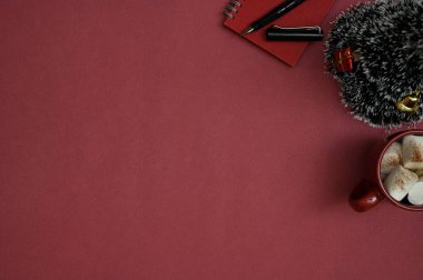 Üst görünüm, Noel temalı kırmızı çalışma alanı ürün veya metin sergisi, küçük Noel ağacı, şekerli sıcak çikolata bardağı ve kırtasiye malzemesi.