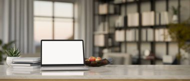 Çalışma alanı masa üstü dizüstü bilgisayar beyaz ekran modeli, elma tepsisi, kitaplar ve dekorla modern parlak odanın bulanık arka planına karşı geniş kitaplık. 3d görüntüleme, 3d illüstrasyon