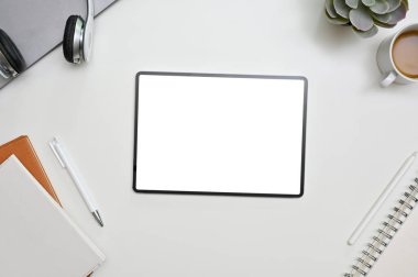 Beyaz masadaki boş ekran tabletli, kitaplı ve kırtasiyeli beyaz ekran çalışma alanının üst görünümü 