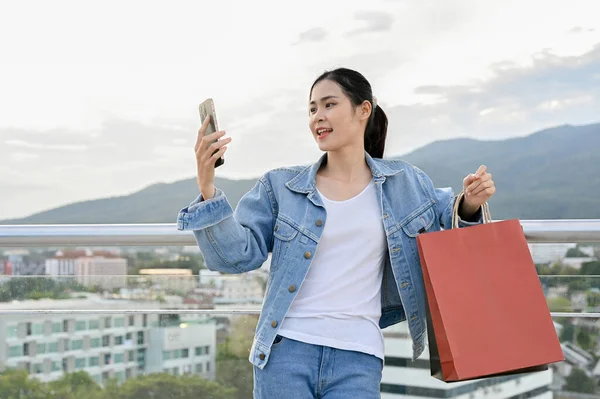 Atractiva Confiada Joven Asiática Usando Teléfono Inteligente Llevando Sus Bolsas — Foto de Stock