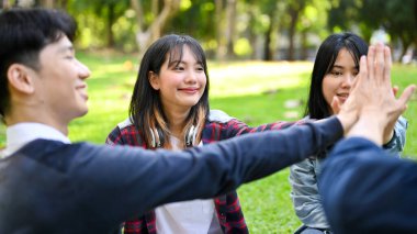 Neşeli Asyalı genç arkadaşlar takım çalışması olarak el ele tutuşuyorlar. Kutlama, neşe