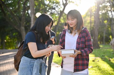 İki güzel ve çekici Asyalı genç üniversite öğrencisi kampüsün parkında yürürken okul projelerini konuşmaktan ve tartışmaktan zevk alıyorlar..