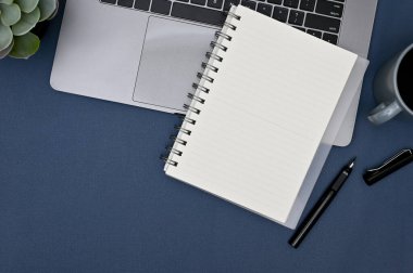 Çalışma alanı boş spiral not defteri, kalem, dizüstü bilgisayar, kahve fincanı ve mavi masa üstü dekor. Üst görünüm, düz uzanma