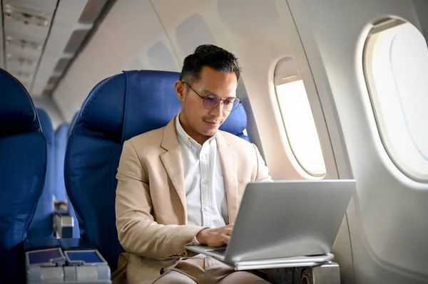 A professional and focused businessman or male CEO using a laptop computer, typing on the keyboard, managing his business tasks during the flight.