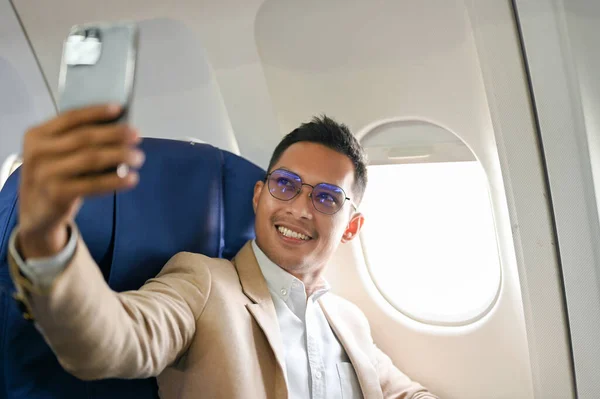 Successful and handsome Asian businessman or CEO taking his picture with smartphone during the flight for an overseas business meeting.