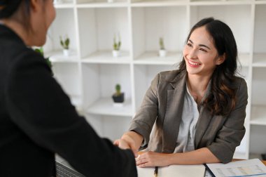 Başarılı ve profesyonel Asyalı iş kadını iş birliği toplantısında iş ortağıyla el sıkışıyor ve gülümsüyor..