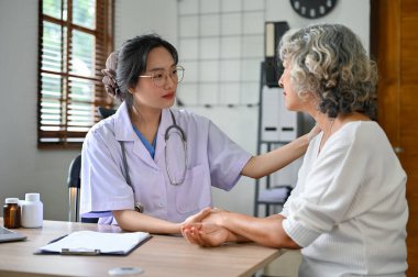 İlgili bir Asyalı kadın doktor, hastanın sağlık kontrolü sırasında elini tutar ve onu rahatlatır. sağlık hizmeti kavramı
