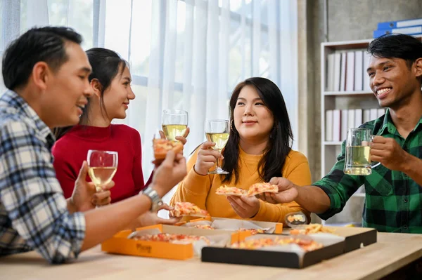 Group of happy and joyful Asian coworkers enjoy talking, having fun time together, drinking wine and eating pizza in the office. Corporate new year party