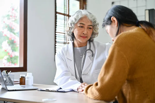 Professional and caring Asian aged female doctor talking, having a serious conversation with her young patient in the hospital office.