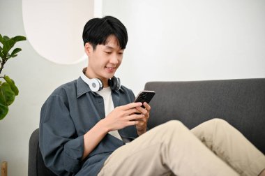 Yan manzara, mutlu ve rahat Asyalı genç adam oturma odasında kanepede dinlenirken arkadaşlarıyla telefonda sohbet ediyor..