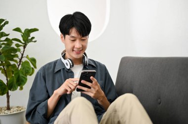 Yakışıklı Asyalı genç adam oturma odasındaki kanepede dinlenirken arkadaşlarıyla telefonda sohbet ediyor..