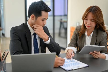 Profesyonel ve zeki Asyalı iş adamı veya erkek CEO kadın bir muhasebeciyle çalışıyor, rapordaki mali verileri birlikte kontrol ediyorlar..