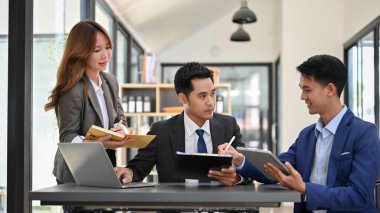 Bir grup Asyalı profesyonel iş adamı toplantı odasında iş finans stratejilerini tartışıyor ve beyin fırtınası yapıyorlar..