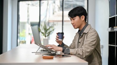 Yan görünüş, yakışıklı ve zeki Asyalı genç erkek programcı ya da serbest grafik tasarımcı kafede çalışıyor, laptop bilgisayar kullanırken kahveyi yudumluyor..