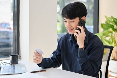 Çevrimiçi alışveriş yapan genç bir adamın, elinde akıllı telefon ve kredi kartı tutarken kredi kartı çağrı merkeziyle telefon görüşünü kapatın. 