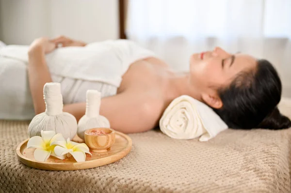 selective focus, Spa herbal balls and salt body scrub on massage table with a lady relaxes lying on massage table. Thai massage concept