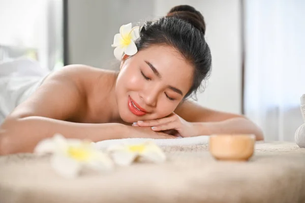 Beautiful, calm and peaceful young Asian woman lying on massage table with eyes closed in beauty spa salon. massage, spa, body care, aromatherapy, therapeutic