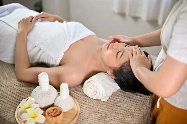 Calm and peaceful Asian woman getting facial treatment massage by a professional masseur in the spa salon.