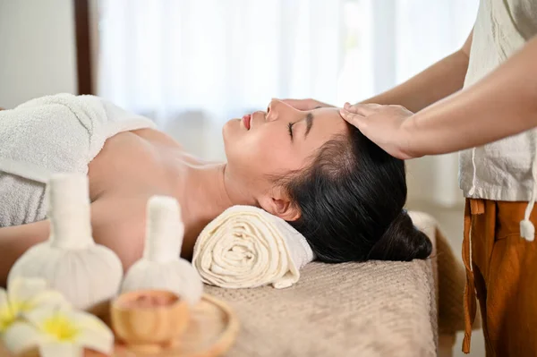 Calm and peaceful Asian woman getting facial treatment massage by a professional masseur in the spa salon. Wellness lifestyle. side view